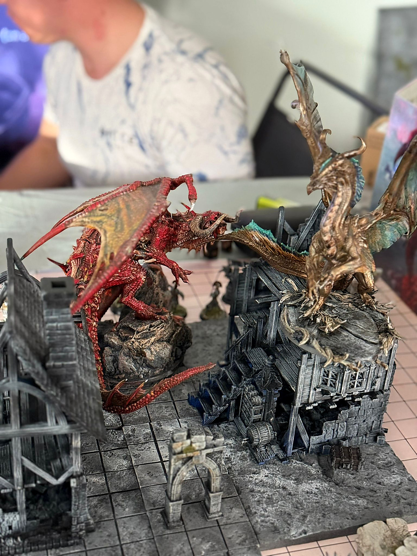 A red dragon and a gold dragon clashing above ruined buildings