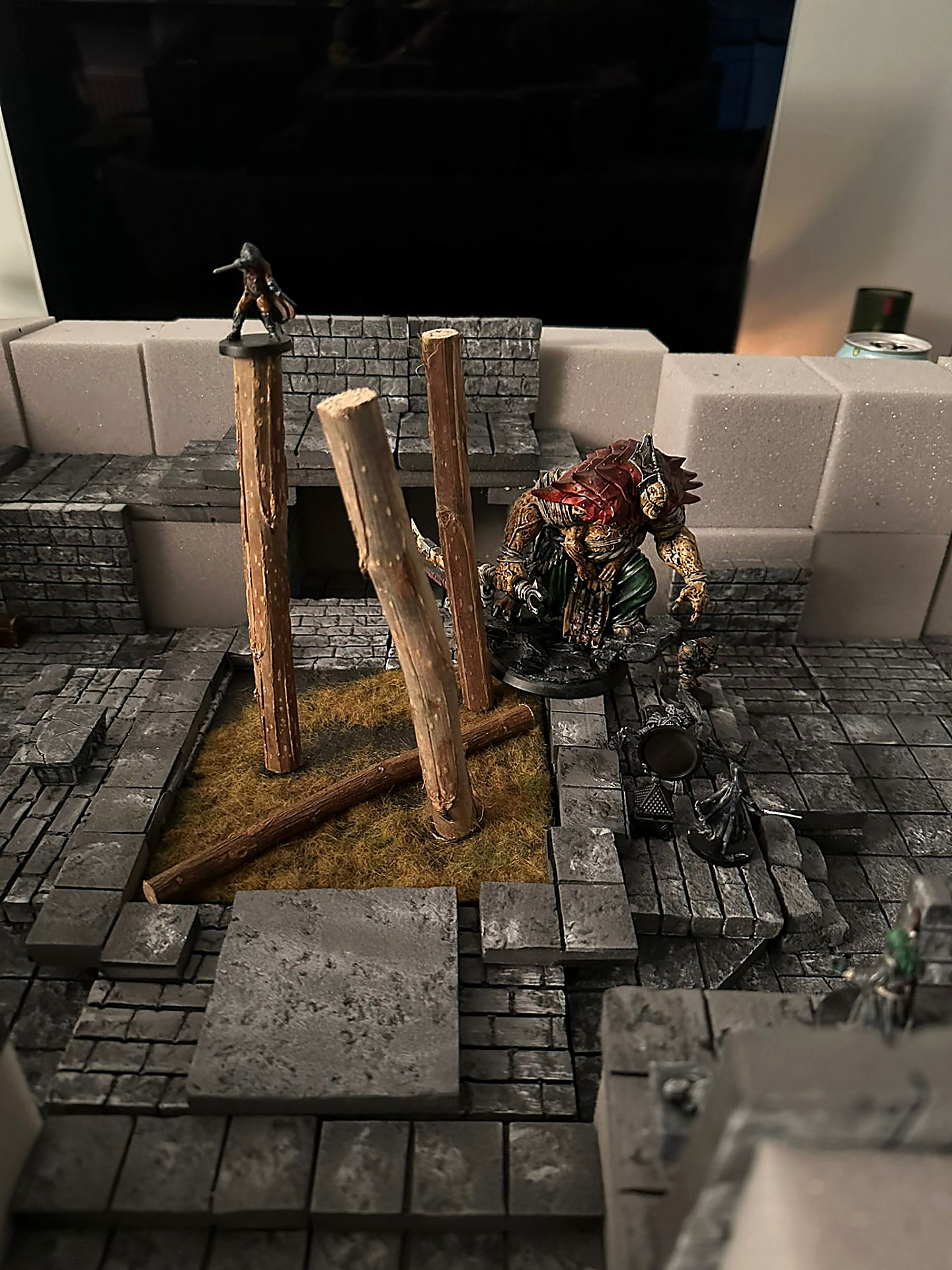 A hulking red-scaled monster rising from a pit beside broken pillars