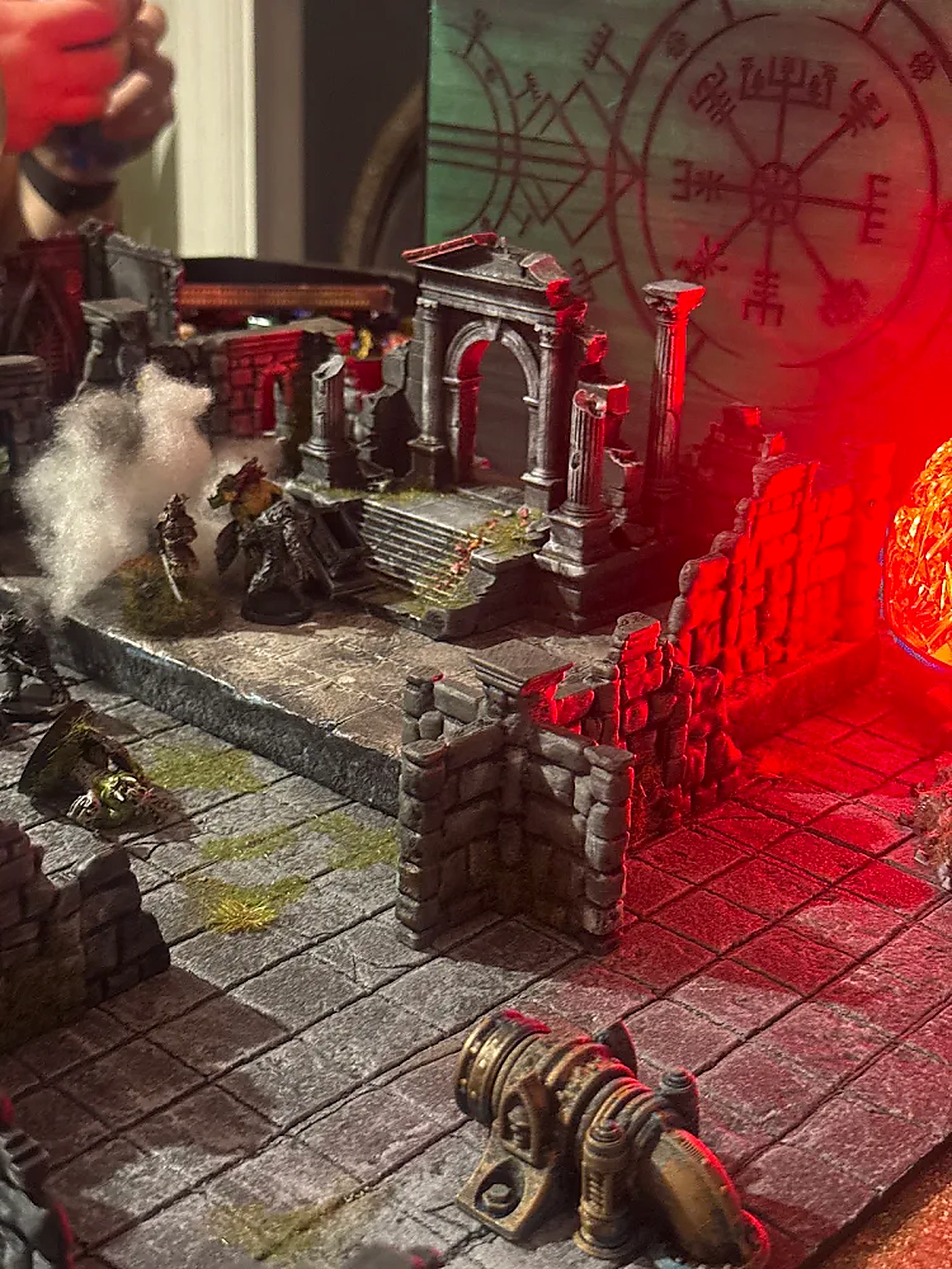 Red-lit ruined temple terrain with miniatures and a cannon in the foreground